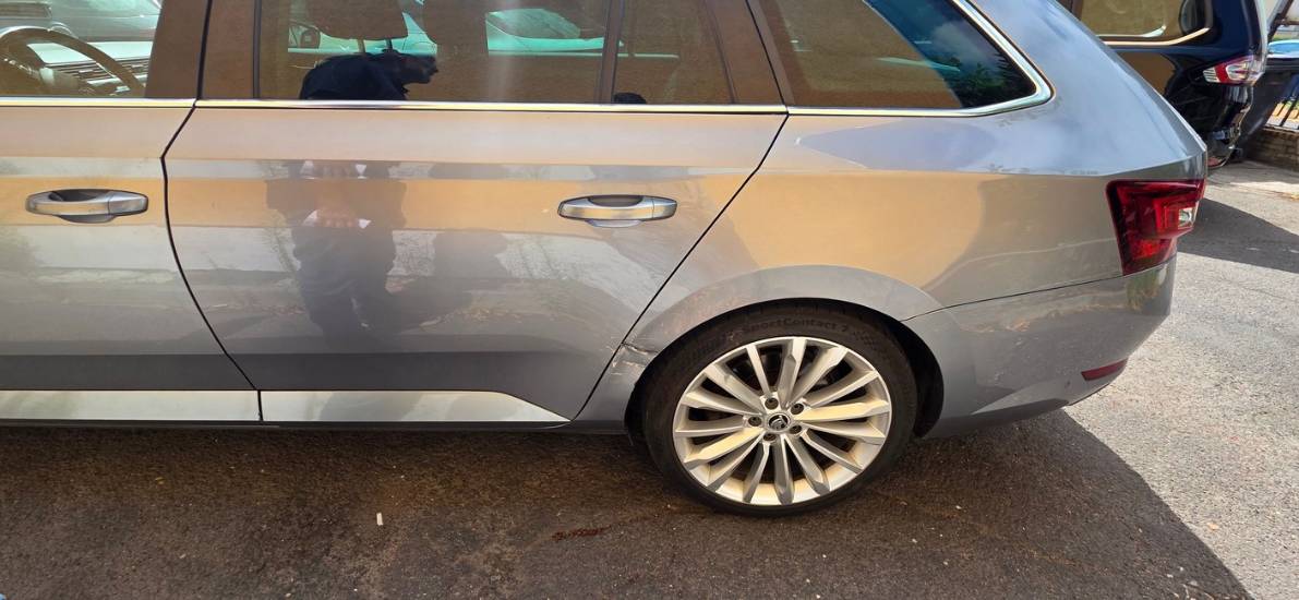 Vedere laterală anonimizată a unui Skoda Superb cu avarie în zona spate stânga